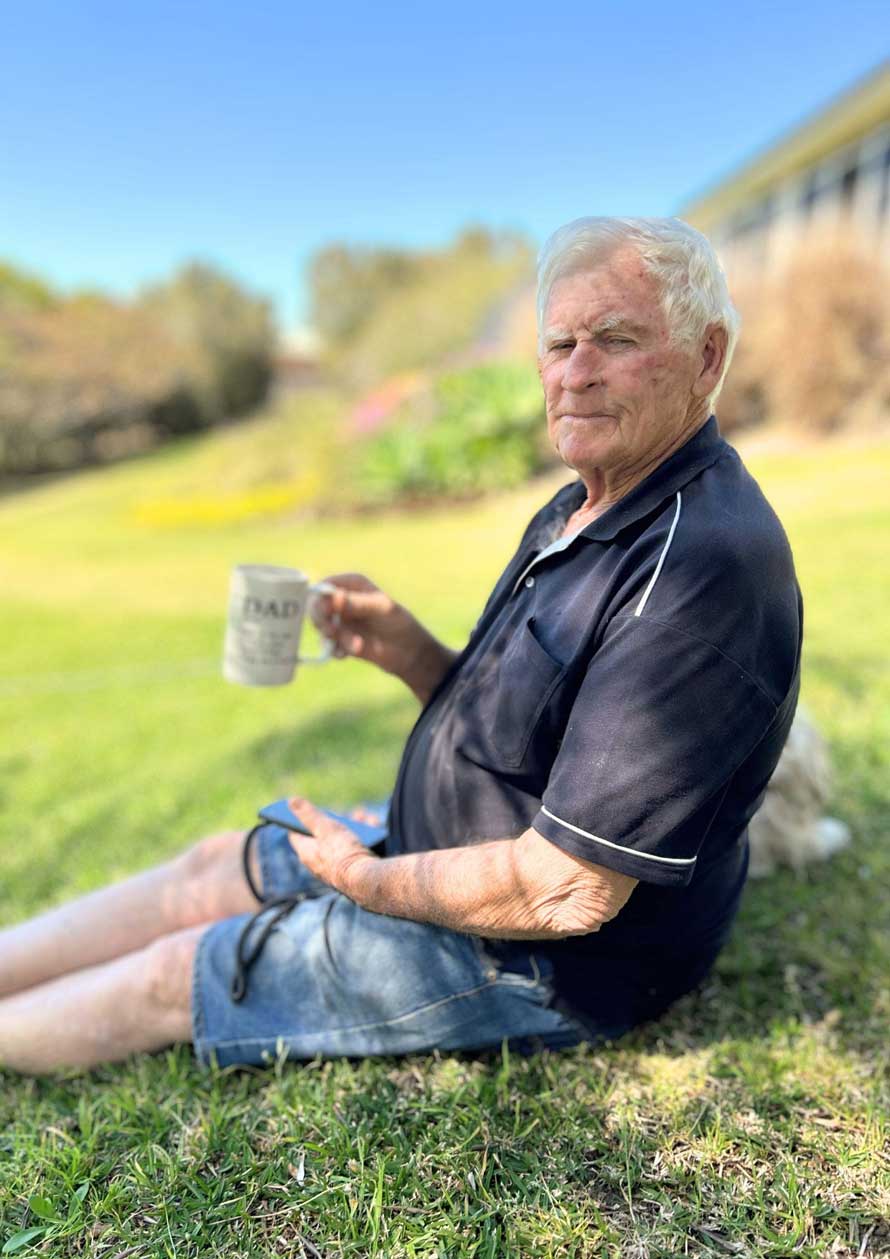 Elderly man enjoying a cup of coffee while sitting on grass.