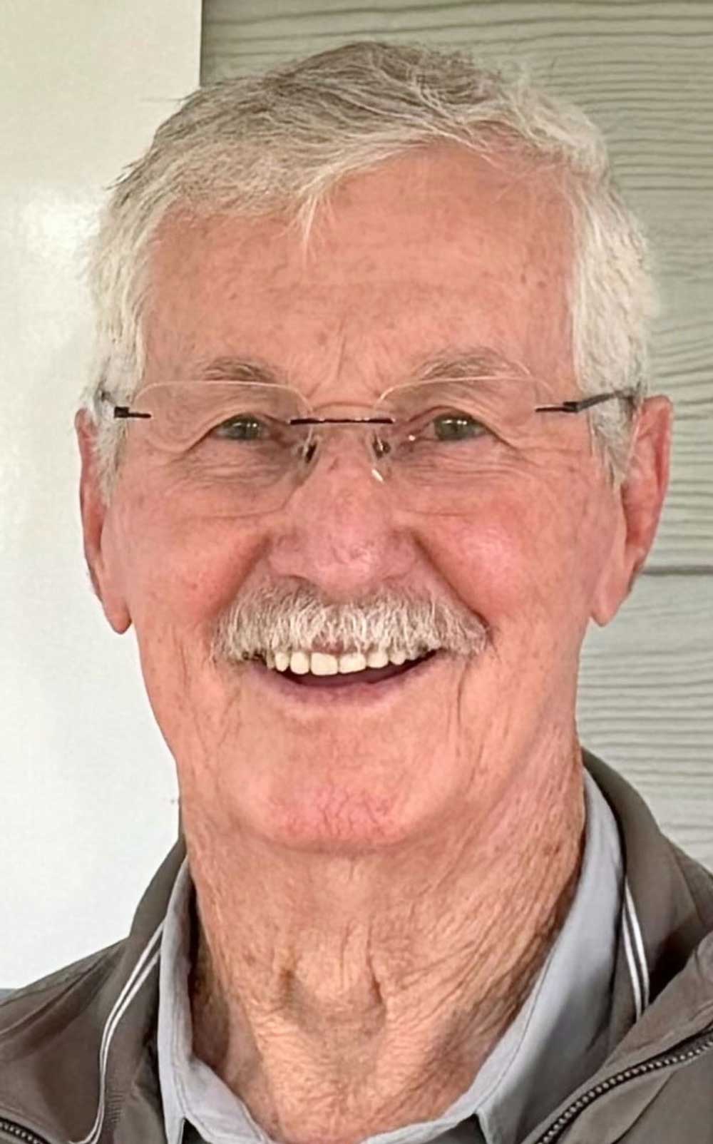 Elderly man with glasses and mustache smiling warmly
