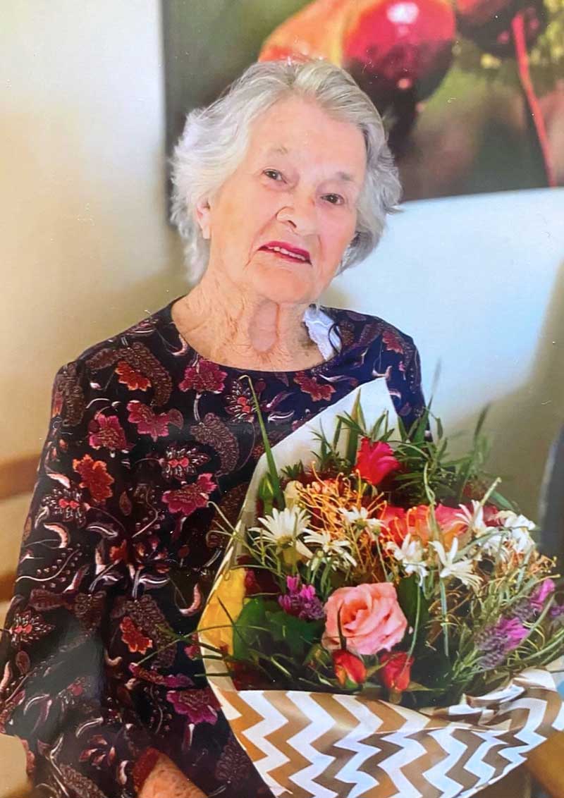 Elderly woman smiling, holding colorful bouquet of flowers.